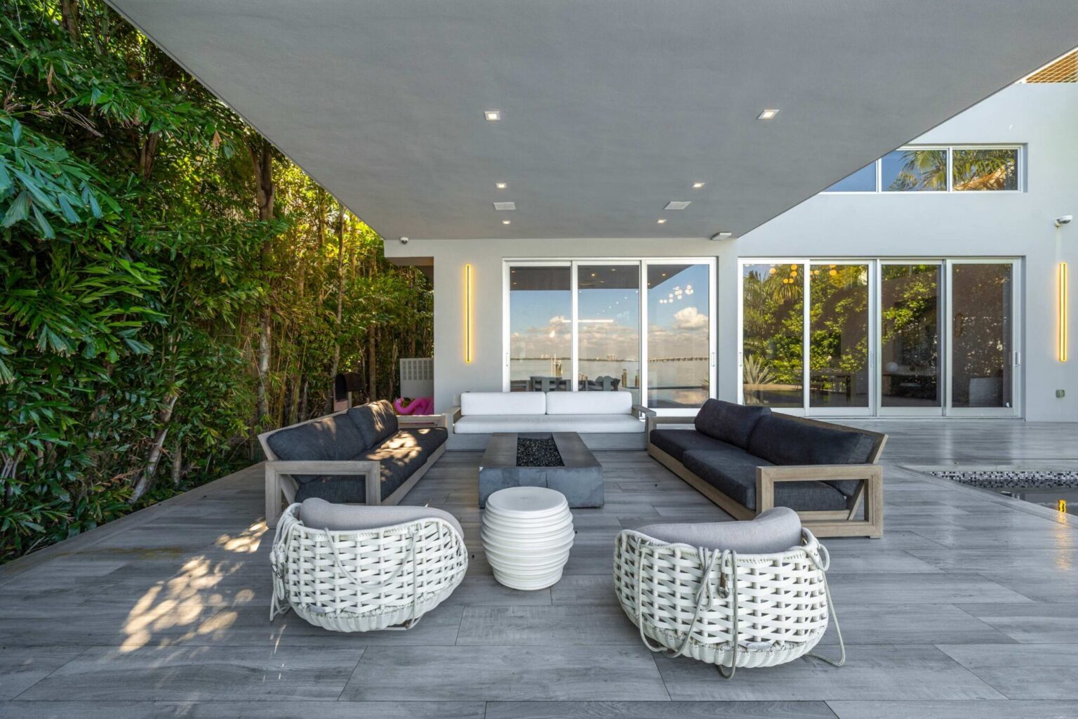 Outdoor lounge terrace featuring contemporary seating, lush tropical landscaping, and seamless indoor-outdoor living. Positioned adjacent to the pool area, this spacious gathering space is designed for relaxation, entertaining, and enjoying the water