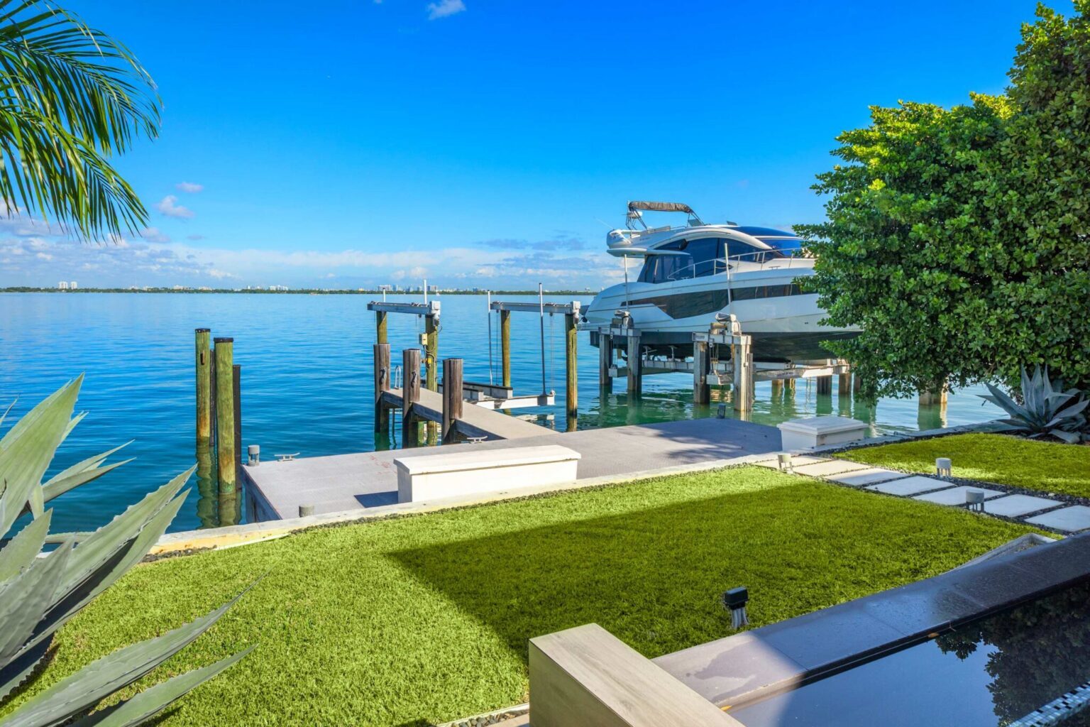 Waterfront lawn and dock area featuring direct bay access, boat lift, and panoramic water views. Landscaped grounds connect the outdoor living spaces to the shoreline, providing convenient access to the property's waterfront amenities.