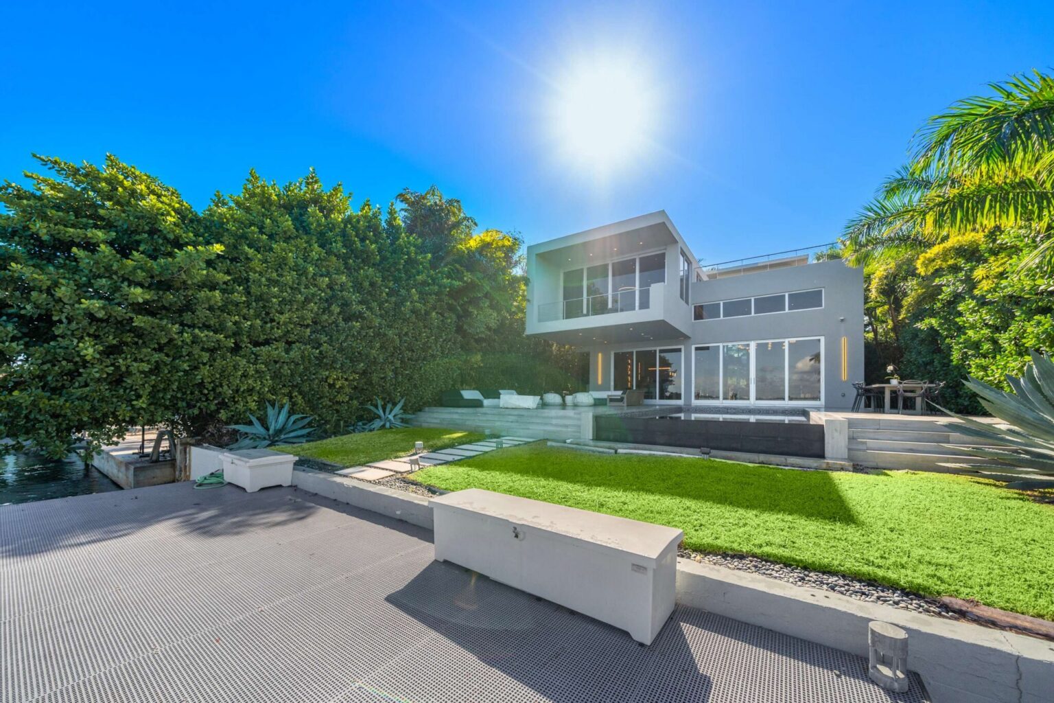 Expansive waterfront backyard featuring a manicured lawn, private pool, sun deck, and tropical landscaping. Multiple outdoor living areas provide space for lounging, entertaining, and enjoying the private waterfront setting.
