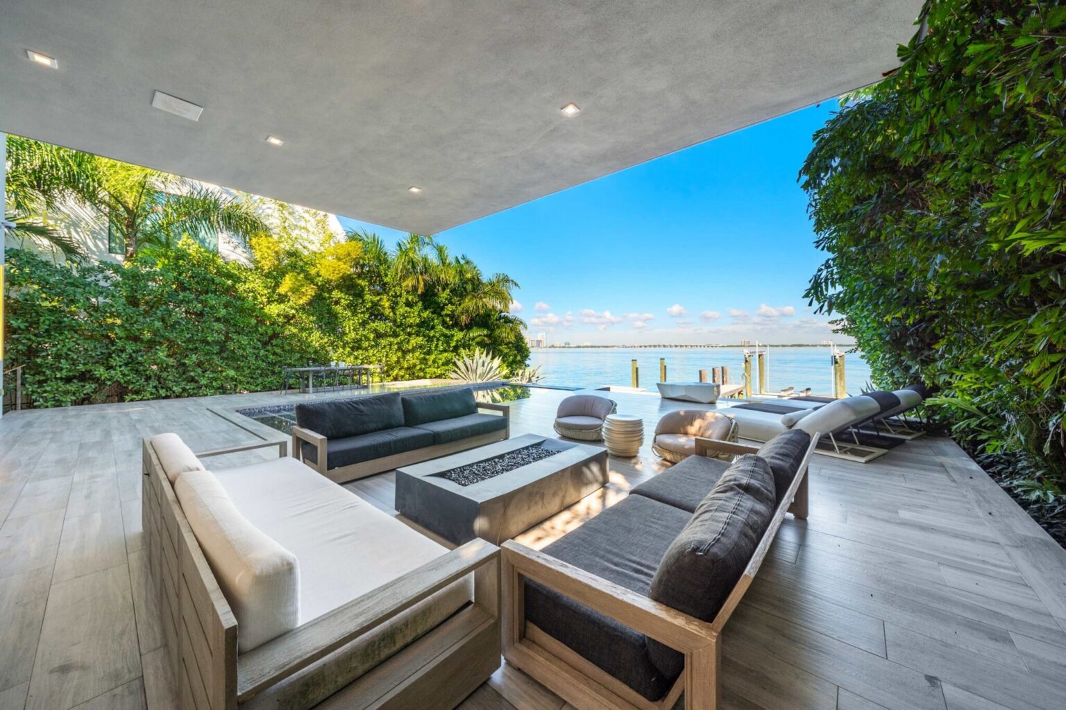 Covered outdoor lounge featuring premium seating, waterfront views, and a spacious terrace. Surrounded by tropical landscaping, this shaded entertaining area offers direct access to the pool deck and private bayfront setting.