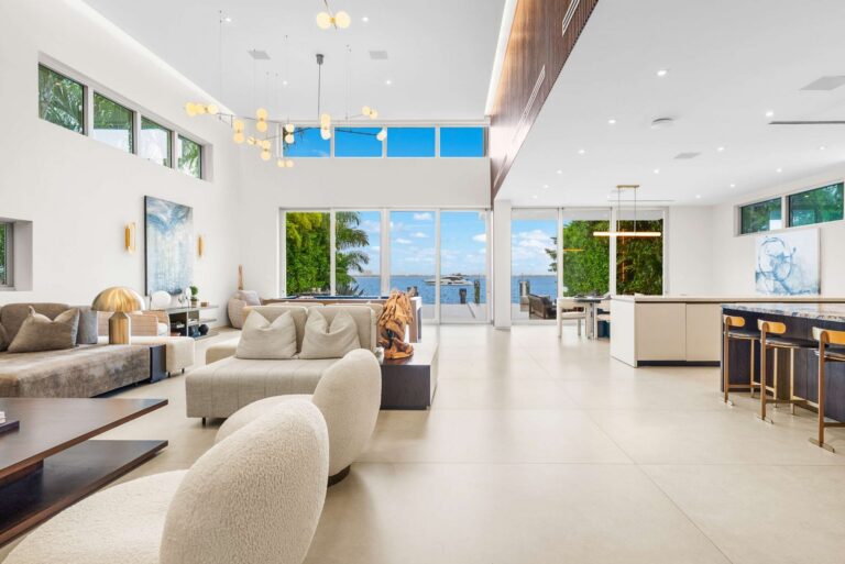Open-concept living area featuring double-height ceilings, floor-to-ceiling glass, waterfront views, designer furnishings, and a modern chef’s kitchen with island seating. Spacious layout designed for entertaining, dining, and indoor-outdoor living.