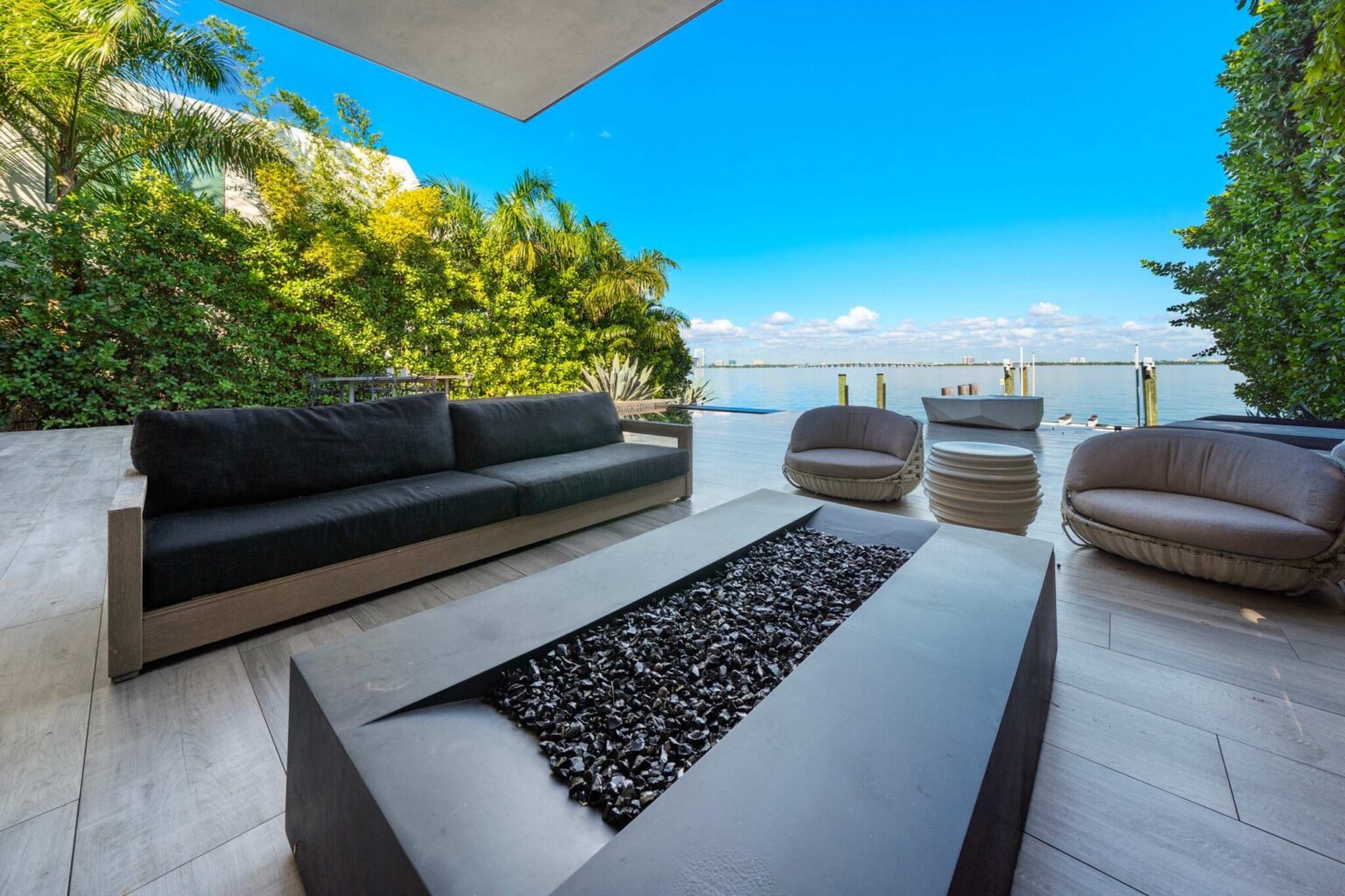 Bayfront lounge area featuring contemporary outdoor seating, panoramic water views, and tropical landscaping. Positioned along the waterfront, this private terrace offers a comfortable setting for relaxation and enjoying the surrounding scenery.