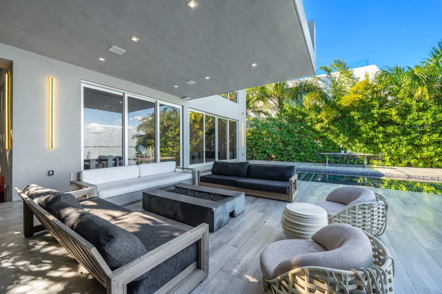 Waterfront terrace featuring contemporary lounge seating, tropical privacy landscaping, and seamless indoor-outdoor living. Spacious outdoor area designed for relaxation, entertaining, and enjoying the bayfront setting.
