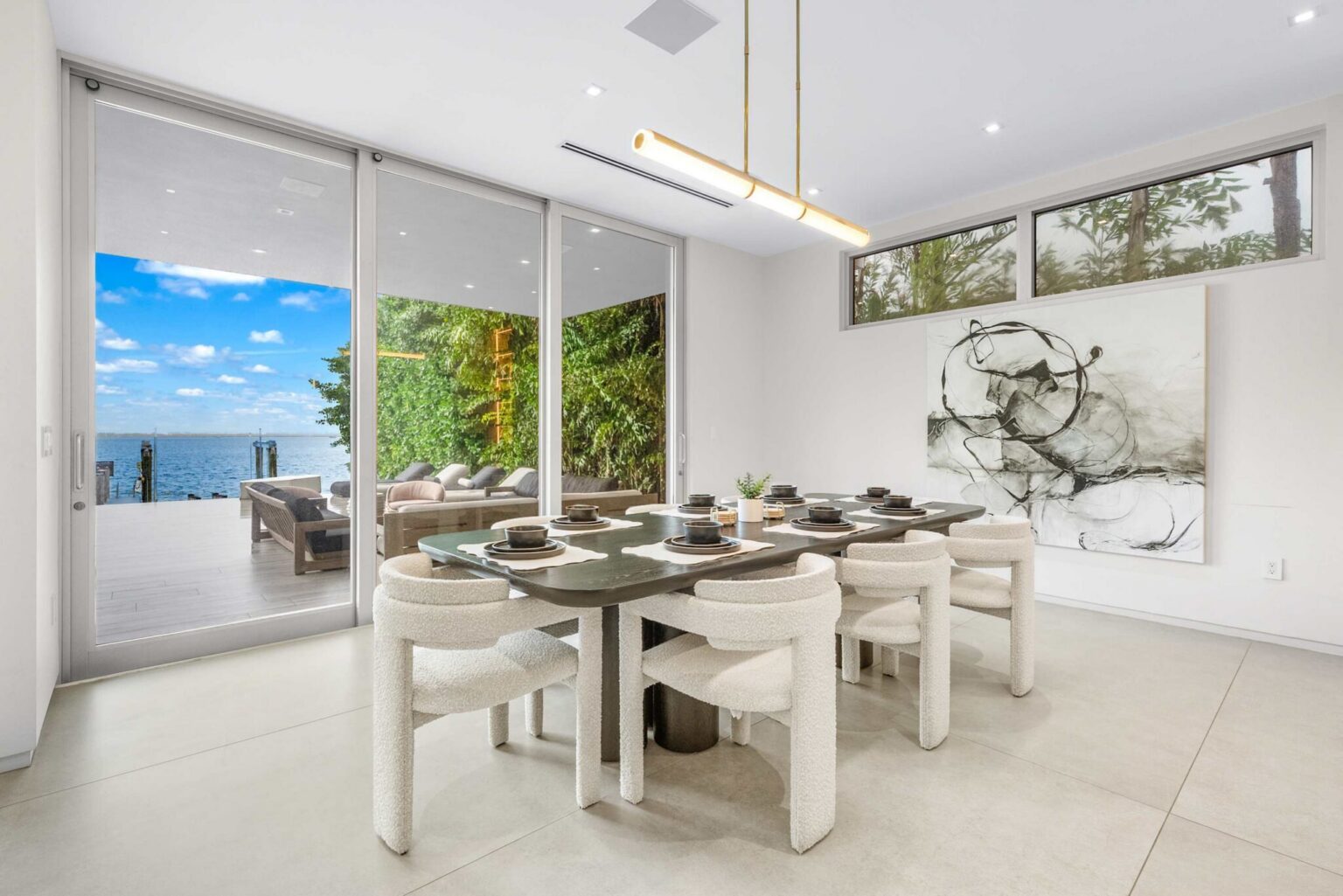 Elegant dining area with floor-to-ceiling glass, waterfront views, and seamless indoor-outdoor living.