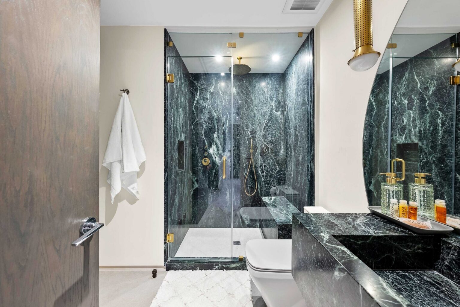 Designer ensuite bathroom featuring a walk-in glass shower, natural stone finishes, custom vanity, and brushed gold fixtures. Contemporary materials, integrated lighting, and premium details create a spacious and functional bathroom layout.