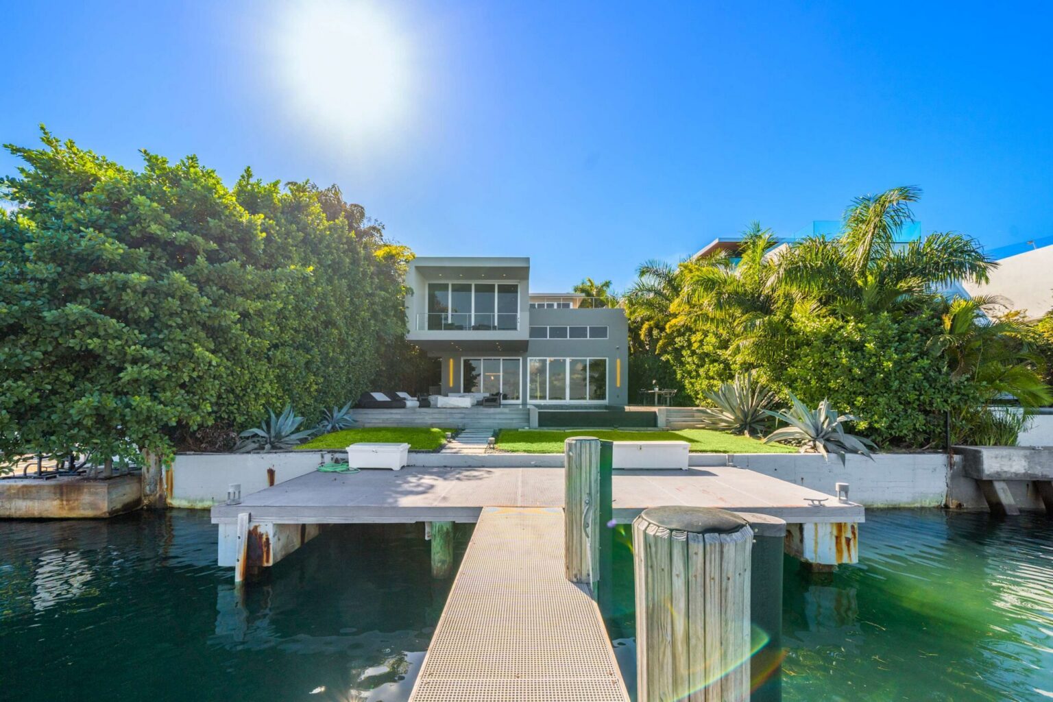 Private dock extending into a protected waterfront canal, offering direct water access and views of the home's pool, lawn, and outdoor living spaces. Lush tropical landscaping enhances privacy throughout the property.
