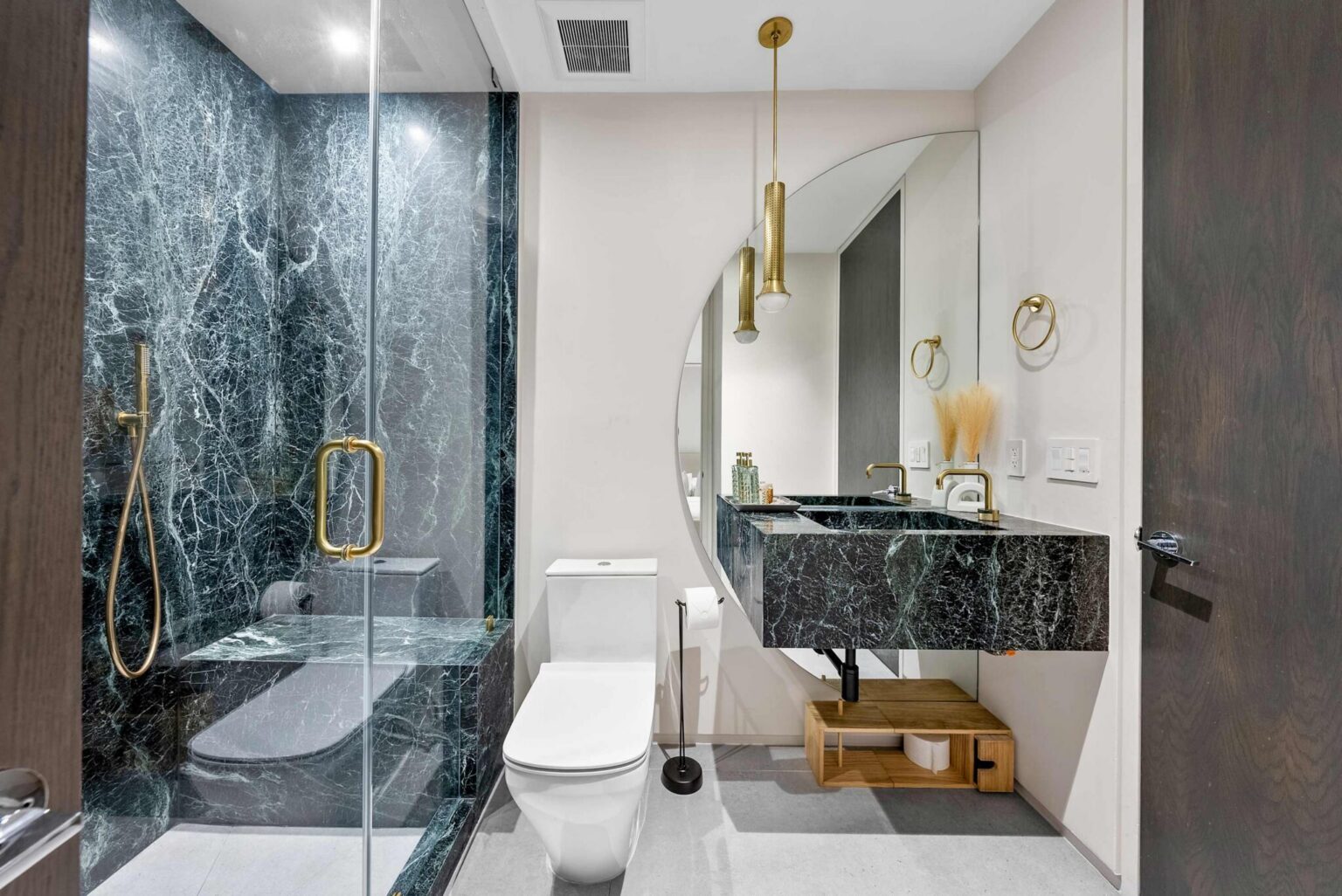 Luxury ensuite bathroom featuring a walk-in glass shower, custom stone vanity, designer lighting, and premium gold fixtures. Natural stone finishes, modern cabinetry, and a spacious layout create a refined and functional bathroom space.