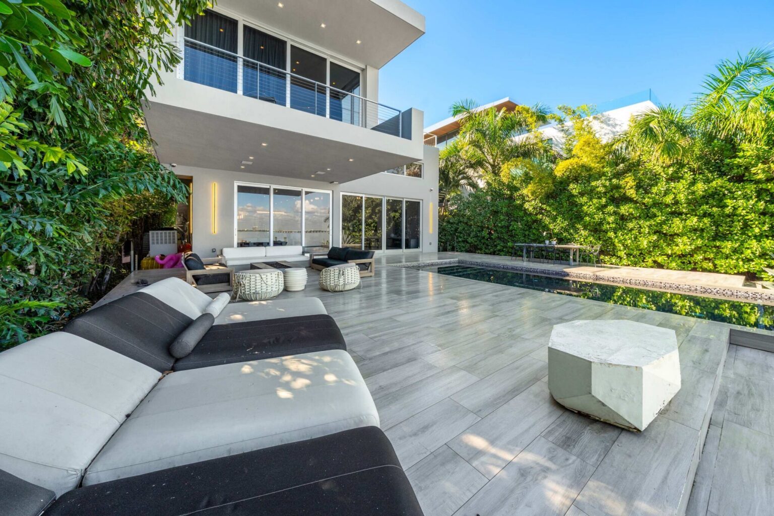 Poolside terrace featuring luxury sun loungers, a private swimming pool, and tropical landscaping. Contemporary outdoor living space with expansive decking, multiple lounging areas, and seamless access to the home's indoor entertaining spaces.