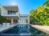 Resort-style backyard featuring a private swimming pool, expansive sun deck, tropical landscaping, and contemporary outdoor living spaces. Floor-to-ceiling glass doors connect the outdoor area to the home's modern interiors, creating seamless indoor