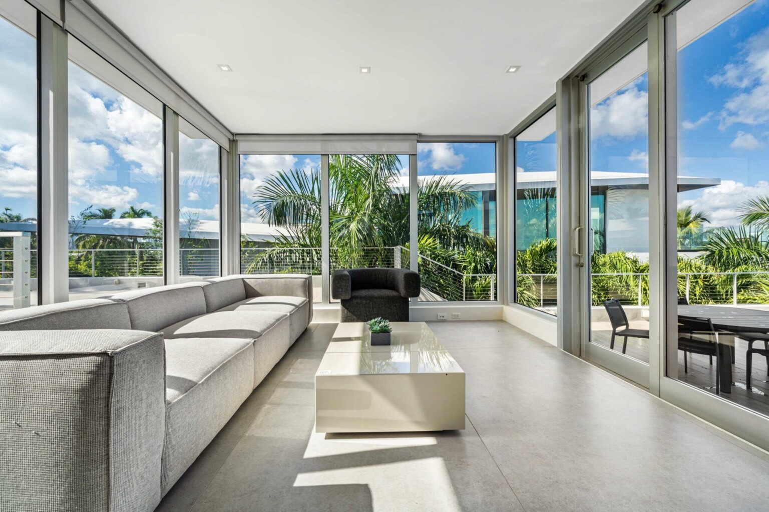 Sun-drenched waterfront lounge wrapped in floor-to-ceiling glass with panoramic tropical views.