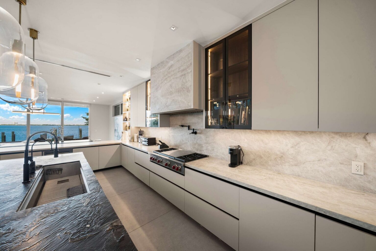 Sleek chef’s kitchen featuring waterfall stone countertops, custom cabinetry, and stunning water views.