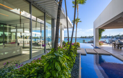 Luxury waterfront Miami villa with floor-to-ceiling glass, tropical landscaping, reflecting pool, and private dock overlooking Biscayne Bay.