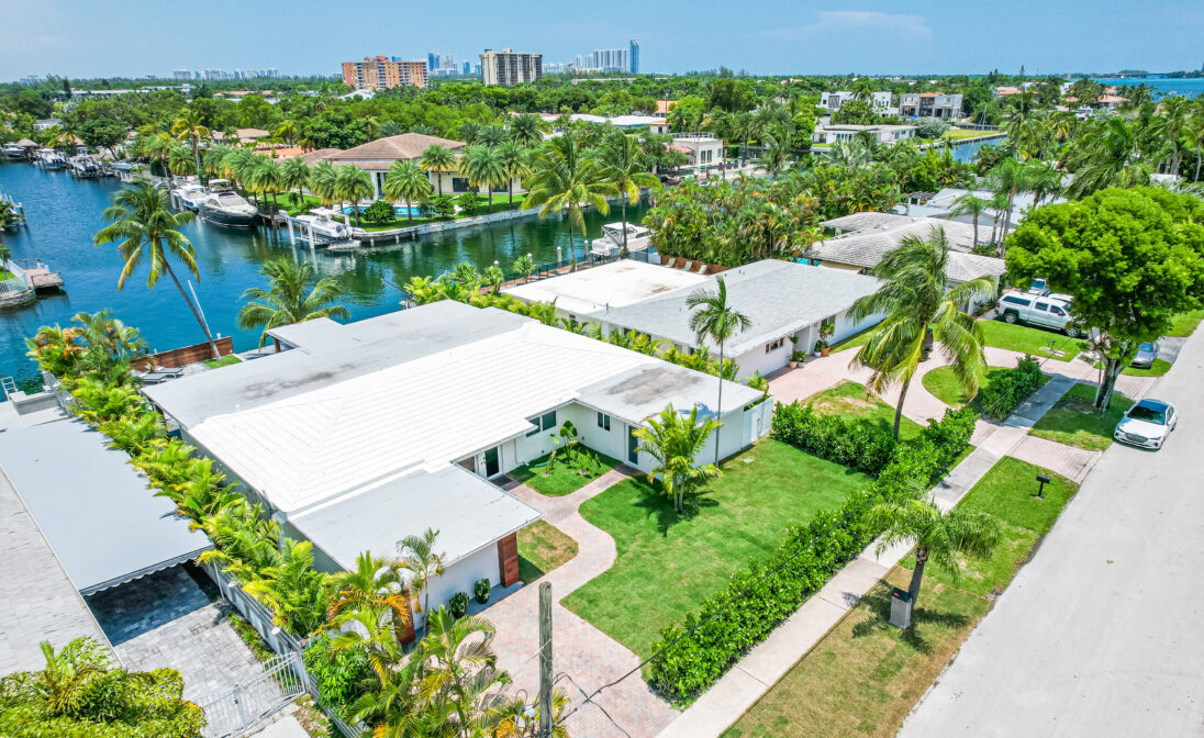 Aerial view of a Miami waterfront neighborhood with homes, palm trees, canals, and lush tropical landscaping.