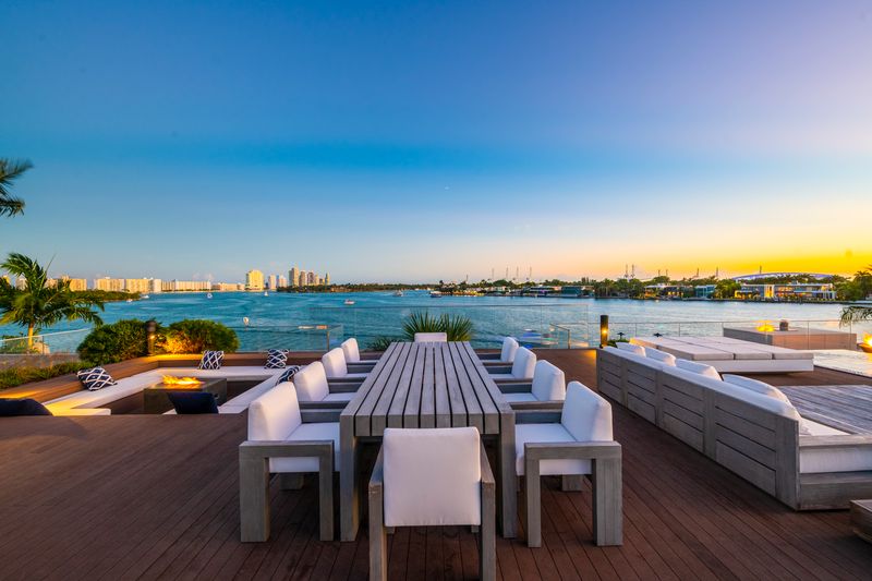 Waterfront Miami villa terrace with outdoor dining, lounge seating, and Biscayne Bay views at sunset.