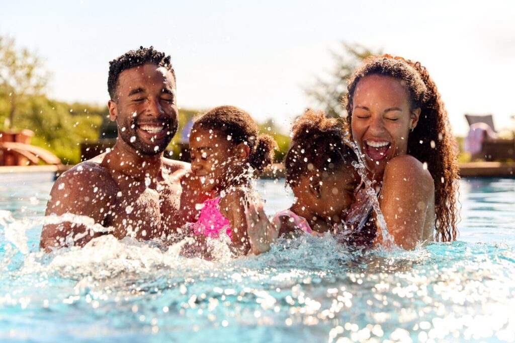 Smiling family of four splashing and playing together in a sunlit swimming pool during a luxury vacation.