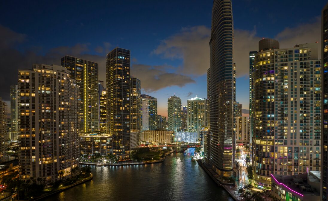 Downtown Miami skyline and waterfront illuminated at night along the Miami River.