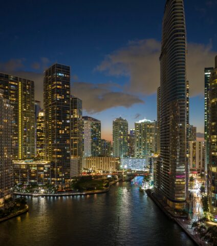 Downtown Miami skyline and waterfront illuminated at night along the Miami River.