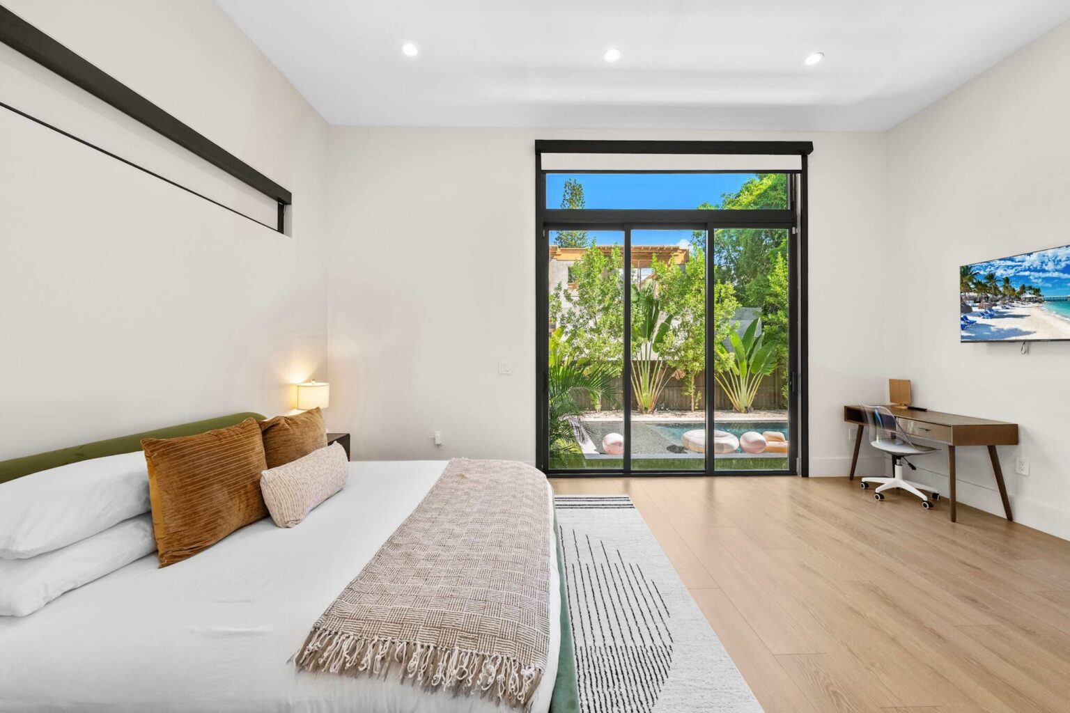 Master bedroom with pool and palm views, desk and wall-mounted TV